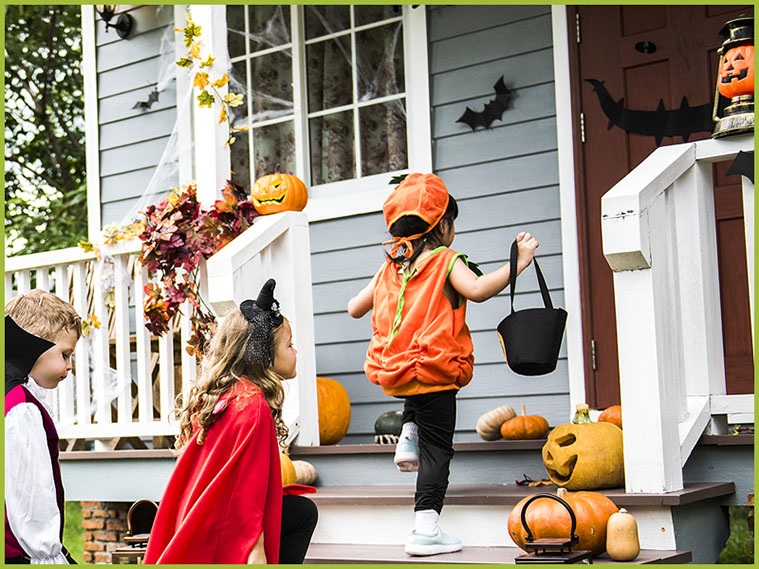 3 kids in costume approaching house decorated for Halloween